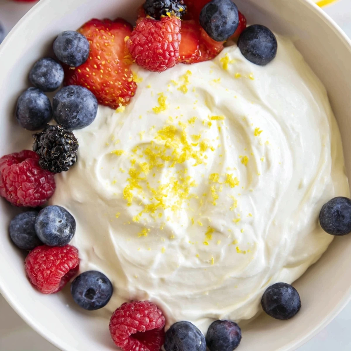 Fluffy cream cheese fruit dip with fresh, colorful berries arranged beautifully for dipping.