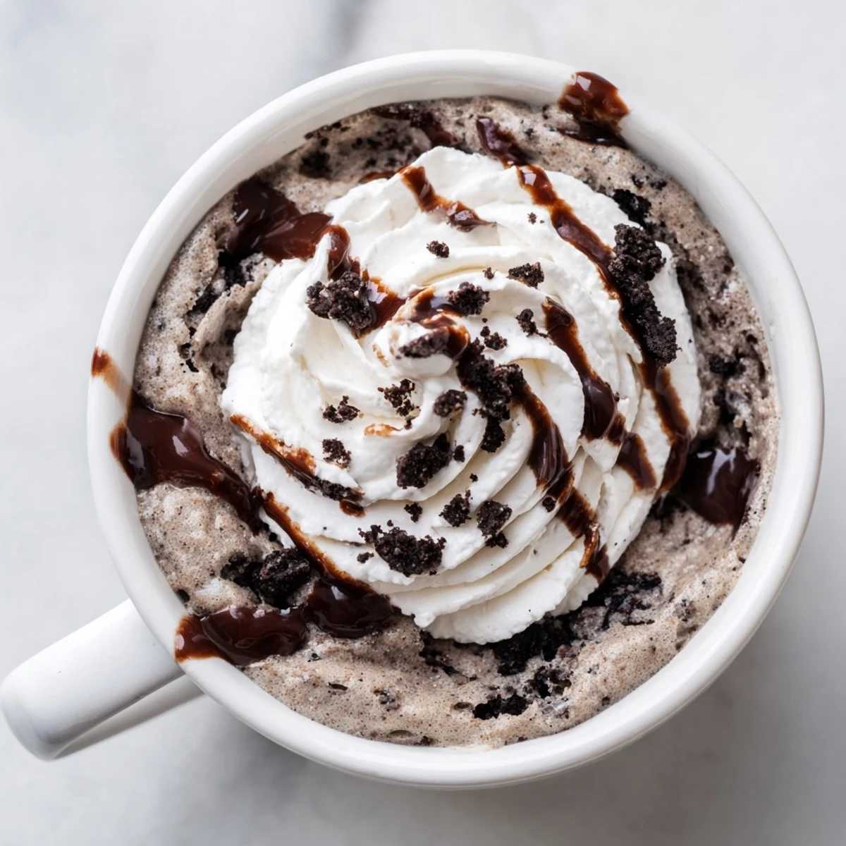 A close-up of a delightful Oreo Mug Cake, topped with whipped cream and crushed cookies.