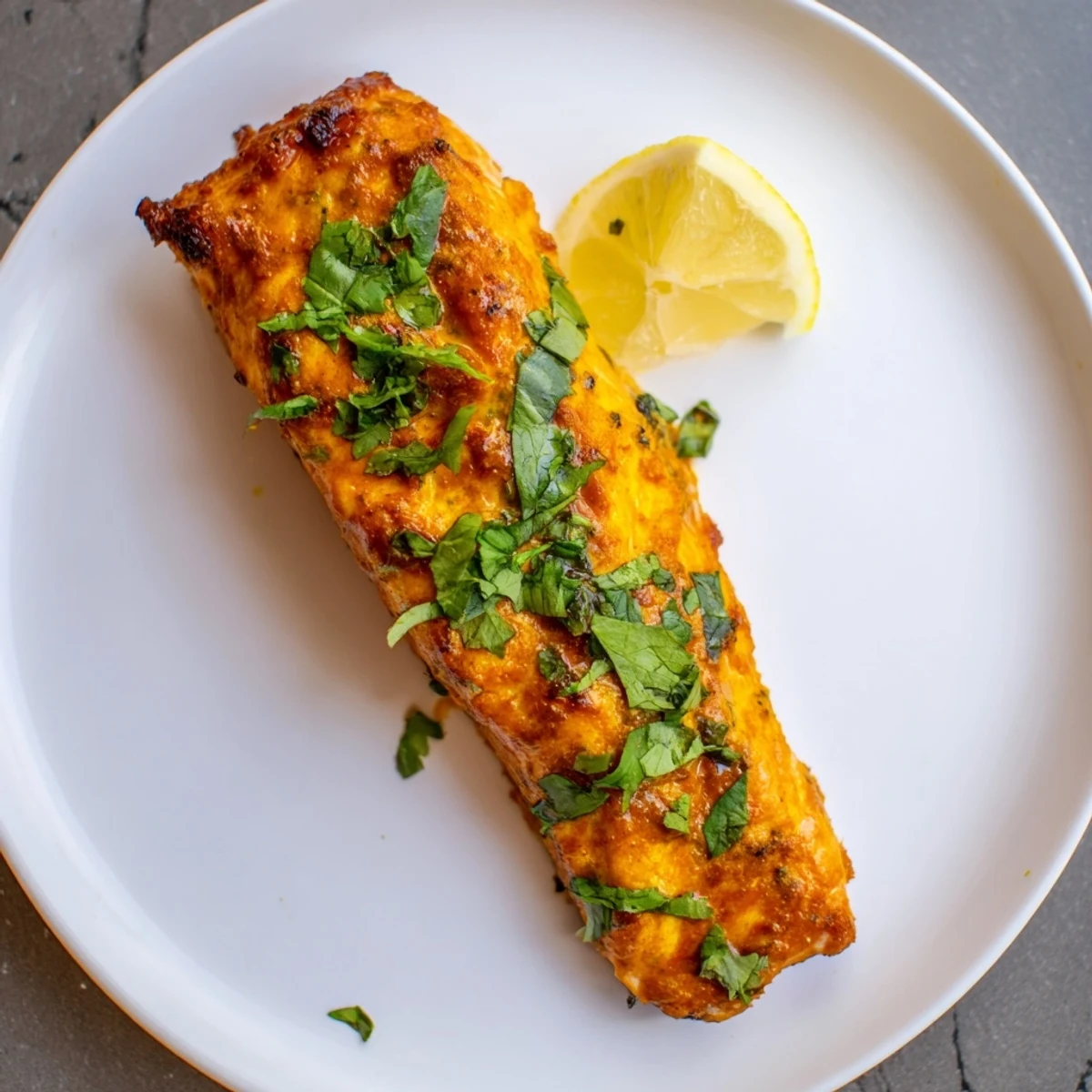 Flaky Indian Tikka Salmon, vibrant red from the spices, is ready to serve with lemon wedges.