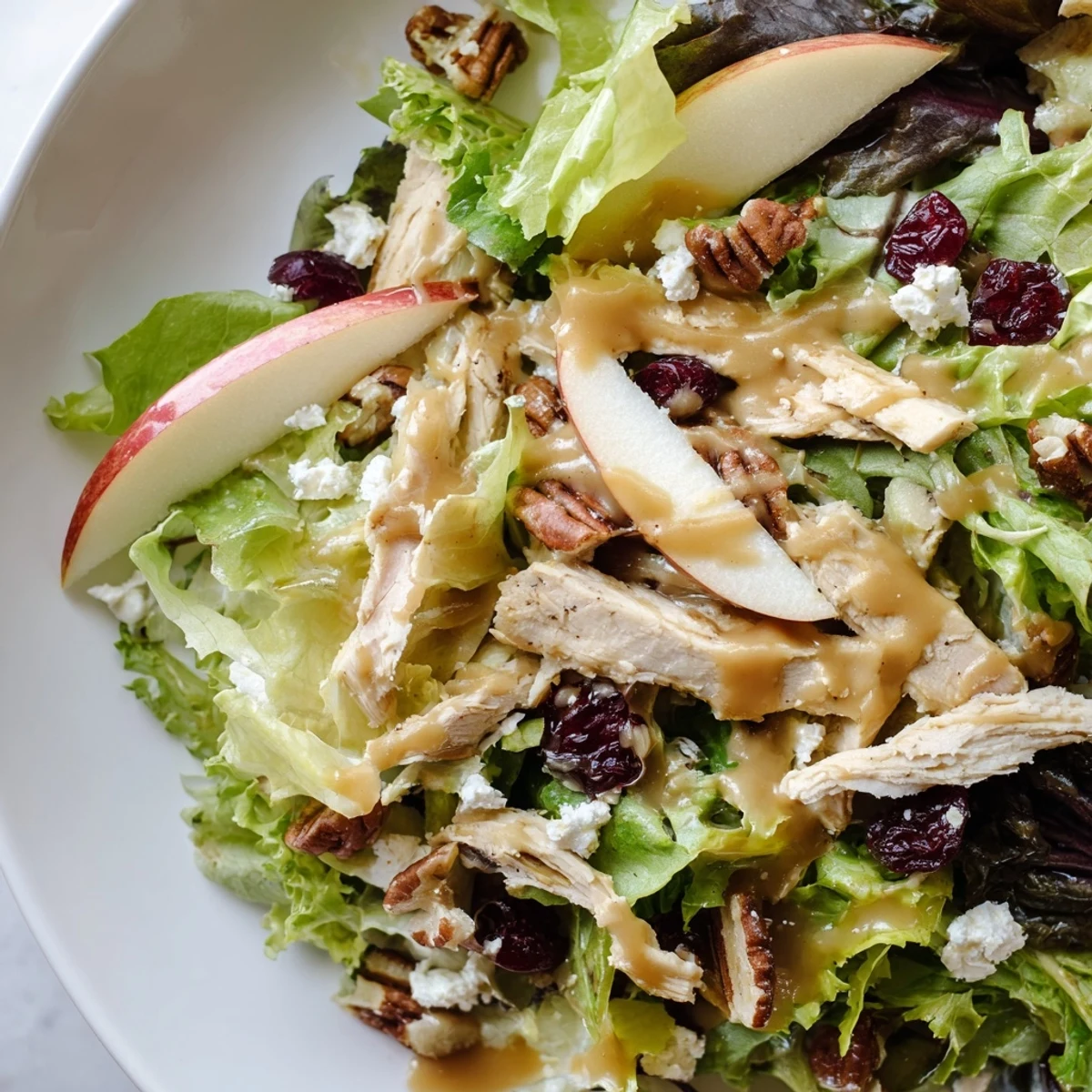 This Caramel Apple Chicken Salad features mixed greens with apples, chicken, and red onion, finished with a sweet caramel-pecan dressing on a white platter.