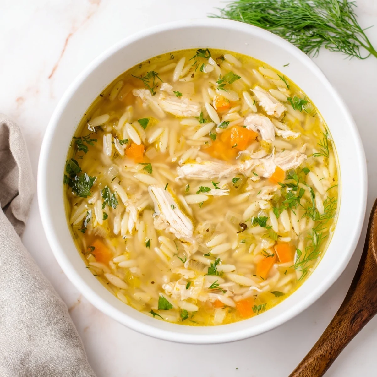 Close-up of Chicken Lemon Orzo Soup with tender chicken, orzo pasta, and vibrant vegetables in a clear broth.