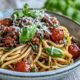 A warm bowl of Italian Drunken Noodles garnished with Parmesan and parsley, served for dinner with a glass of red wine.