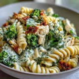 A close-up of protein-rich High Protein Rotisserie Chicken Broccoli Pasta in a skillet, garnished with fresh parsley and extra Parmesan cheese.