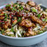Forkful of vibrant Egg Roll Bowls with chicken, crisp cabbage, and shredded carrots, topped with sesame seeds and a spicy drizzle of chili crisp.