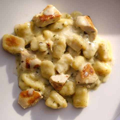 Golden pan-crisped gnocchi and tender chicken bites smothered in a vibrant, creamy basil pesto sauce, served hot and garnished with fresh herbs.  