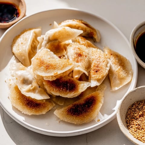 Golden-brown smashed gyozas sizzling in a skillet, served with a small dipping sauce of soy, vinegar, and chili oil.  