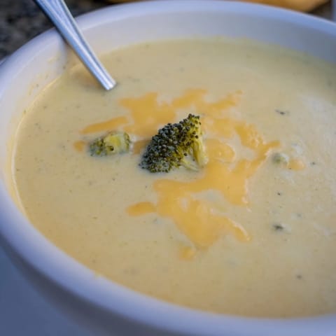 Smooth and velvety homemade broccoli cheddar soup simmering in a pot, with steam rising and melted sharp cheddar blending into the broth.