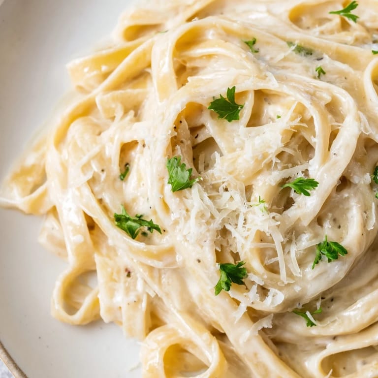 Roasted garlic cream pasta in a skillet, close-up of silky sauce coating al dente noodles.