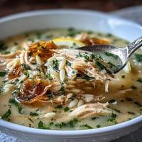 A steaming bowl of Greek lemon chicken soup with tender shredded chicken and orzo in a bright, silky broth.  